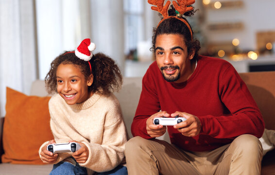 African american family father and daughter laugh and play video games together using a video game console on christmas holiday
