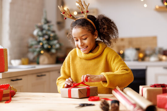 Cheerful ethnic girl decorating gift box on Christmas day