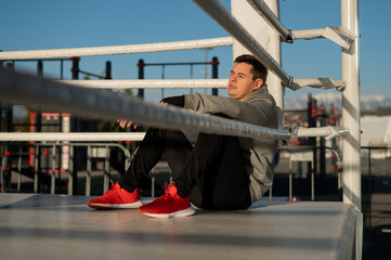 Caucasian male boxer resting in the ring outdoors. 