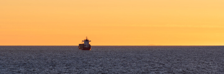 Cargo ship at sea. Beautiful evening seascape. View of the ship at sea at sunset. Sea container transportation. Maritime transport logistics. Wide panorama. Great for backgrounds and designs.