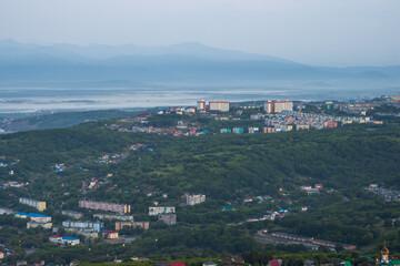 Morning cityscape. Top view of residential urban areas at dawn. Buildings on a hill in the forest. Mountains in the distance. City of Petropavlovsk-Kamchatsky, Kamchatka Krai, Far East of Russia.