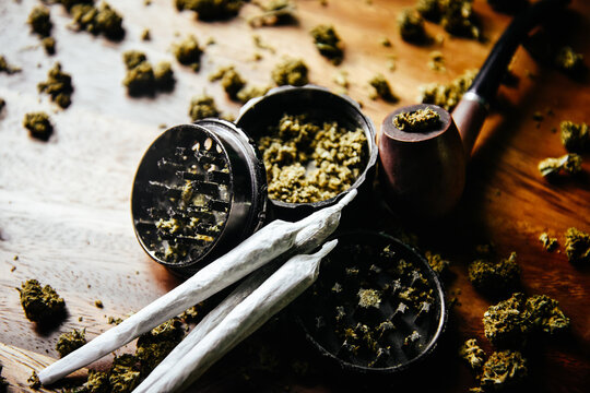 Grinder and joints with marijuana pipe. Drugs and marijuana, marijuana buds. Sativa and indica сbd and tgk on wood. Grass and smoking plants