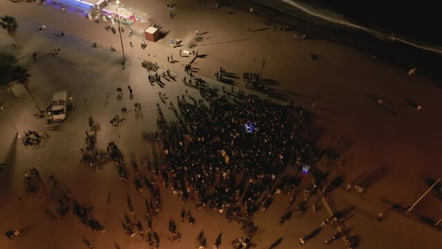 Aerial drone shot above crowd at open-air concert at night on the coast