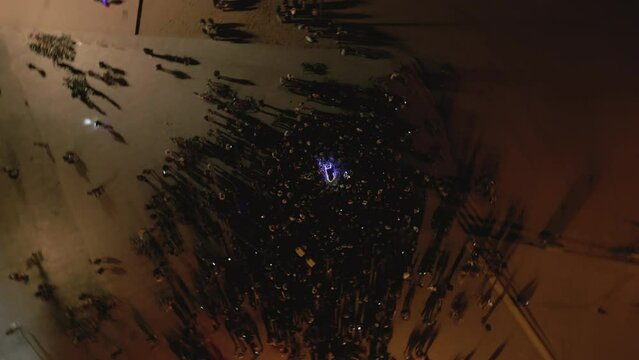 Aerial vertical drone shot above crowd at open-air concert at night on the coast