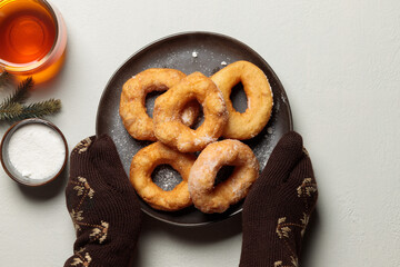 mittened hands hold a plate of donuts. Top view on a light background, with a drink in a cup and fir branches