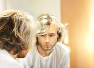 young man looking in the mirror,combing his hair,looking at problems on face.