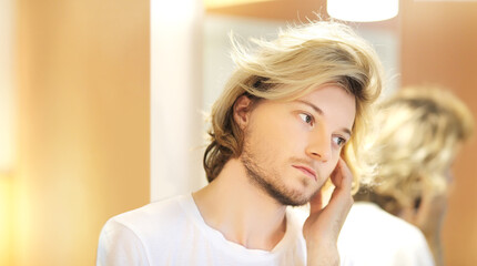Fototapeta premium young man looking in the mirror,combing his hair,looking at problems on face.