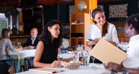 positive female busboy taking order to couple in modern restaurante