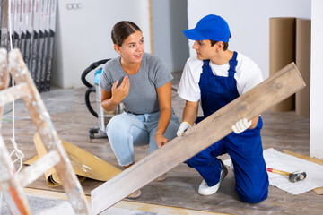 Positive girl interior designer talking to young builder laying click-lock laminate flooring during...