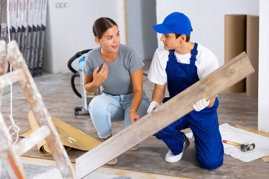 Positive girl interior designer talking to young builder laying click-lock laminate flooring during indoor construction works