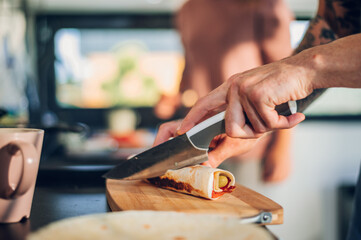 Man hands holding a knife while cutting a burrito made for breakfast