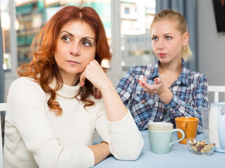 Mature female talking with young daughter at table in home indoors