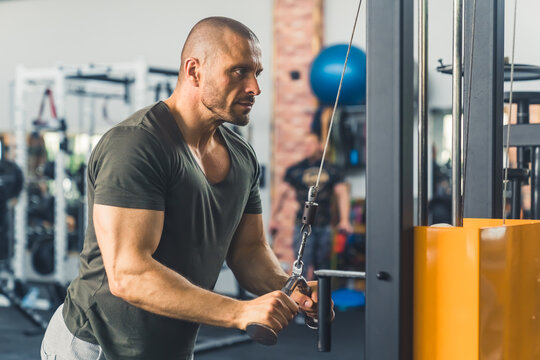 Strong, muscular, handsome bald man, bodybuilder, performing cable tricep extensions in the gym. High quality photo