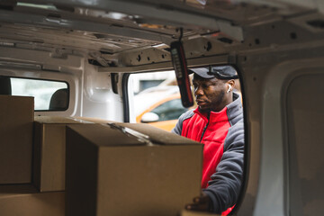 Focused African-American blue-collar-worker - deliveryman - taking out precious cardboard parcels for his clients. Online shopping delivery concept. Van POV. High quality photo