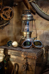 A compass, a pair of motorcycle goggles, and an old lamp on a trunk.	