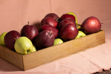 Red and yellow juicy tasty apples in a wooden crate on a pink background