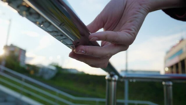 Close-up slow motion of women's fingers touch wet chrome railings. Raindrops flow down the shiny guardrails.