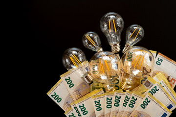 Electricity cost.Light bulbs and euro banknotes on a black background. Rising electricity...