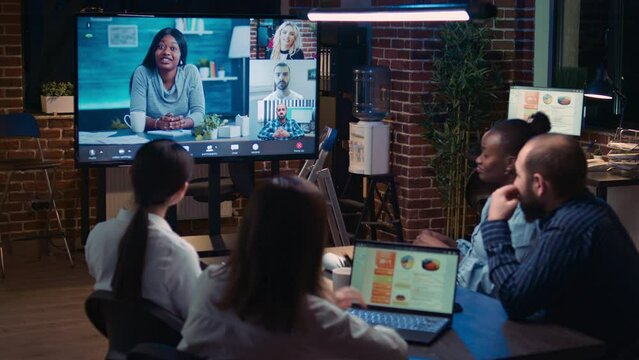 Remote team discussing analytics report in business meeting videocall, diverse employees talking in videoconference at night time. Office workers chatting in teleconference, brainstorming