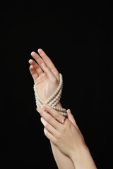 Young woman with elegant pearl jewelry on black background, closeup