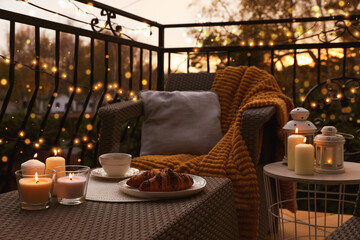 Beautiful view of garden furniture with pillow, soft blanket and burning candles at balcony - obrazy, fototapety, plakaty