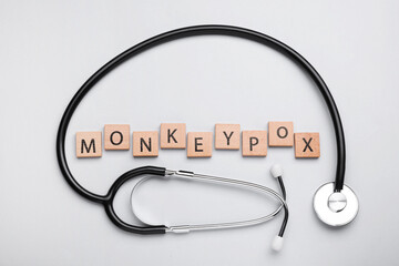 Word Monkeypox made of wooden cubes and stethoscope on light background, flat lay