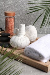 Herbal massage bags, spa stones, sea salt and rolled towel on grey table