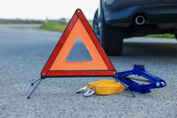 Emergency warning triangle, towing strap and scissor jack near car outdoors. Safety equipment - obrazy, fototapety, plakaty