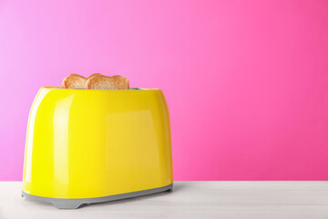 Modern toaster with slices of roasted bread on white wooden table. Space for text