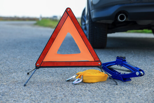 Emergency warning triangle, towing strap and scissor jack near car outdoors. Safety equipment