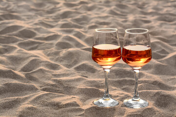 Glasses of tasty rose wine on sand, space for text