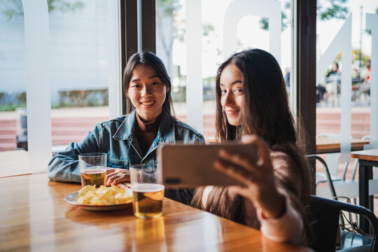 Two young women taking a selfie with the smart phone while sitting in a bar