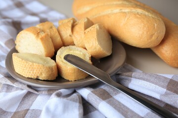 Whole and cut baguettes with fresh butter on checkered tablecloth, closeup