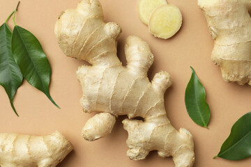 Fresh ginger with green leaves on light pale brown background, flat lay