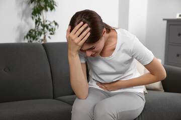 Young woman suffering from cystitis on sofa at home - obrazy, fototapety, plakaty