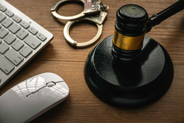 Concept of internet crime with gavel, computer keyboard, mouse and handcuff on a wooden background.