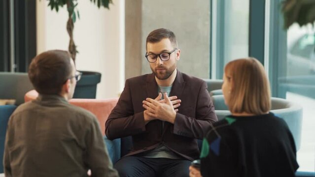 A solid man in a business suit and glasses refuses to take cash from a young couple.