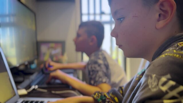 Bored kids playing video games on computers near barred windows on sunny day