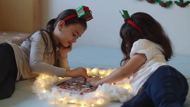 A beautiful caucasian girl lying on the bed opens and takes out candy from the cell of the advent calendar wrapped in a burning garland with cotton wool, side view close-up with slow motion.
