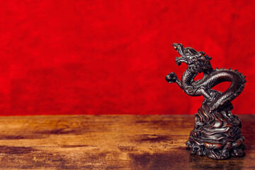 Carved wooden Asian Tibetan dragon statue against red background on wooden table for Chinese lunar new year right side