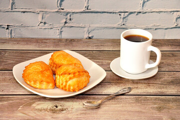 A plate with three buns stuffed with cottage cheese and a cup of hot coffee on a wooden table.