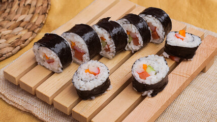 Close up a set of fresh and cheap japanese sushi rolls with crabstick, cucumber, carrot and sausage served on a wooden board