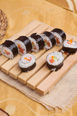a set of fresh and cheap japanese sushi rolls with crabstick, cucumber, carrot and sausage served on a wooden board