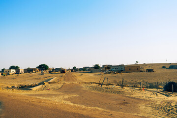 Obraz premium Empty road approaching remote desert village inside the desert. Distant horizon, Hot summer at Thar desert, Rajasthan, India.