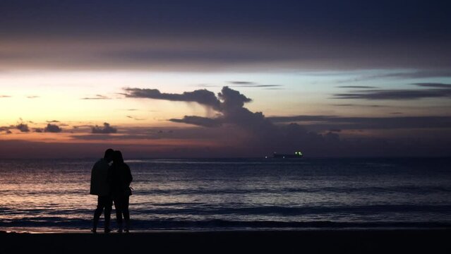 Silhouette of a couple walking on the beach at sunset. Honeymoon romantic couple