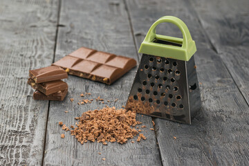 Milk chocolate and a metal grater on a wooden table.