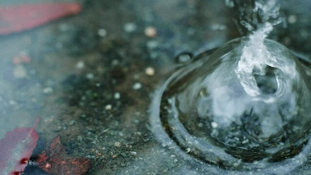 梅雨、公園の砂利の地面の水たまりに雨の水滴が落ちて波紋を残すスローモーション