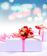 white gift boxes with red-gold ribbon and bokeh background.