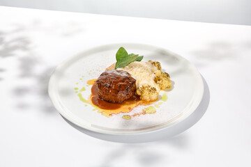 Beef cutlet with grilled cauliflower with gravy and cheese sauce on white plate. Elegant beefsteak on light background with shadows of sunlight. Summer menu with hard shadows Meat ball of minced meat