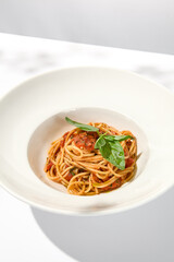 Vegetarian pasta with basil and tomatoes on white plate. Tomato pasta in summer menu with hard shadows Spaghetti with tomatoes on light background. Vegan food - spaghetti marinara